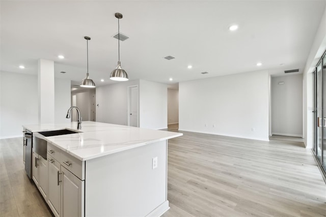 kitchen featuring pendant lighting, light stone counters, an island with sink, and light hardwood / wood-style flooring