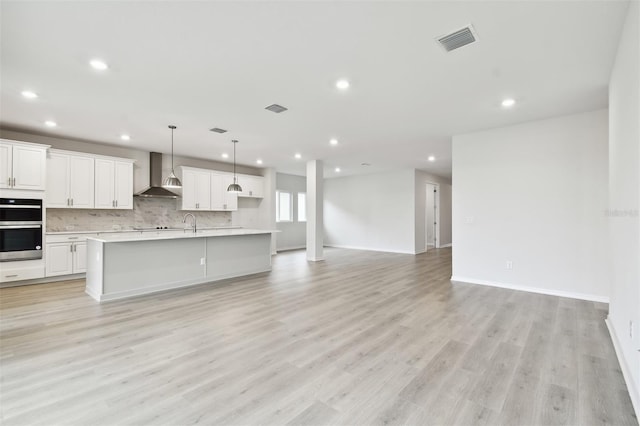 kitchen with light wood-type flooring, wall chimney exhaust hood, stainless steel double oven, pendant lighting, and white cabinets