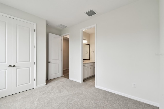 unfurnished bedroom featuring light carpet, ensuite bathroom, and a closet