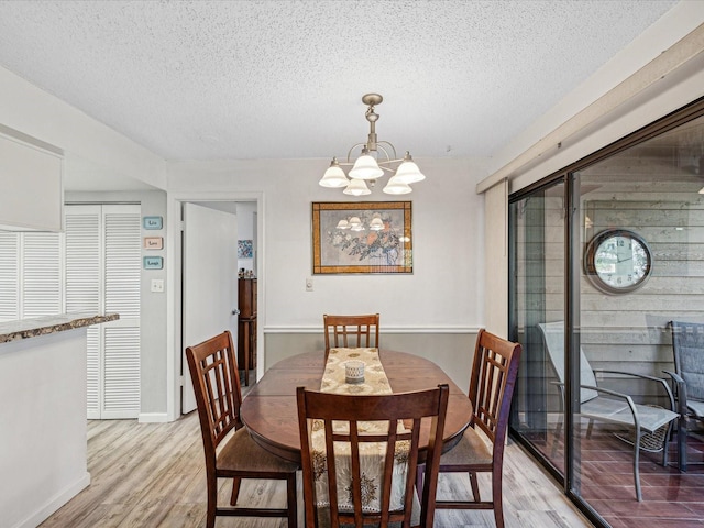 dining space featuring a textured ceiling, light hardwood / wood-style floors, and an inviting chandelier