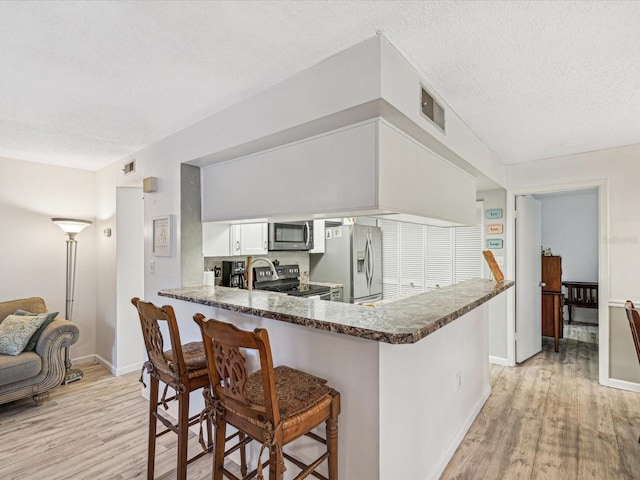 kitchen featuring stainless steel appliances, kitchen peninsula, light hardwood / wood-style floors, a textured ceiling, and white cabinets