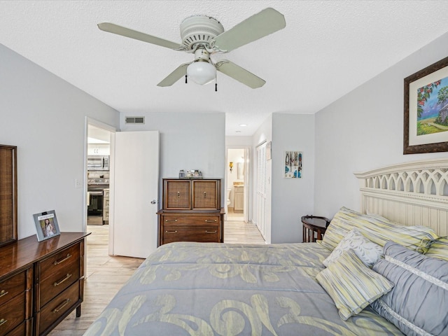 bedroom featuring ceiling fan, a textured ceiling, connected bathroom, and light hardwood / wood-style flooring