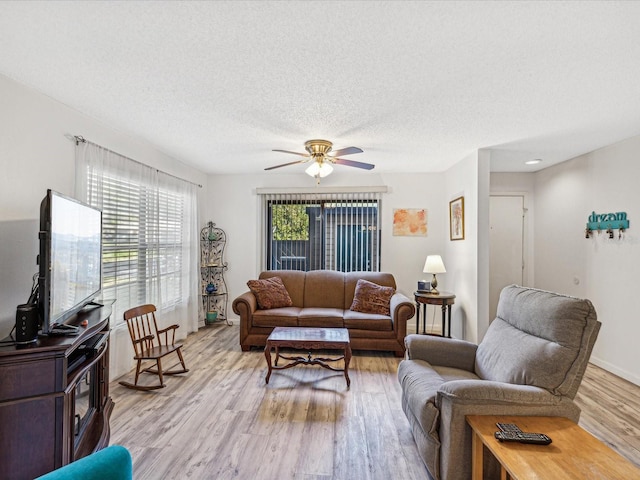 living room featuring ceiling fan, light wood-type flooring, and a textured ceiling