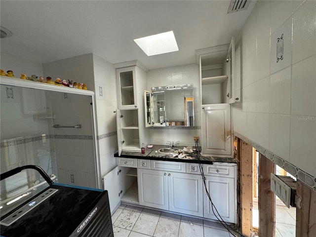 kitchen with a skylight, decorative backsplash, sink, and white cabinets