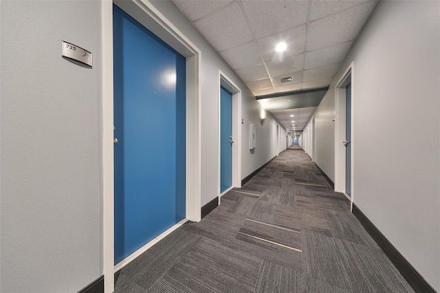 hallway with a paneled ceiling and dark carpet