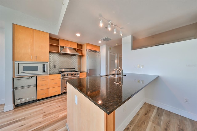 kitchen featuring sink, kitchen peninsula, built in appliances, dark stone countertops, and light hardwood / wood-style floors