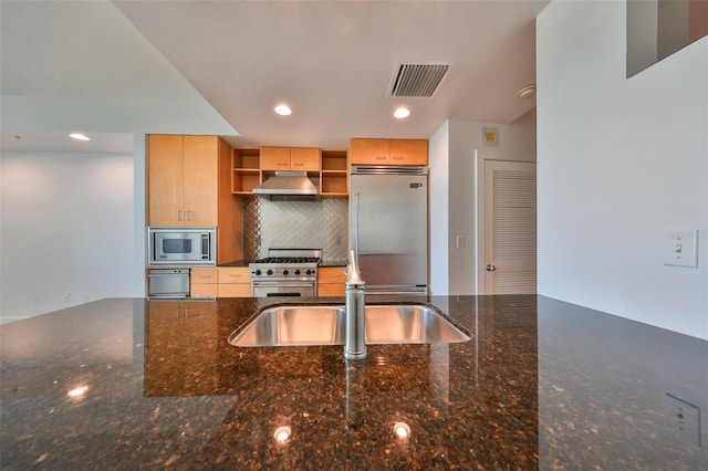 kitchen featuring backsplash, built in appliances, dark stone countertops, and light brown cabinets