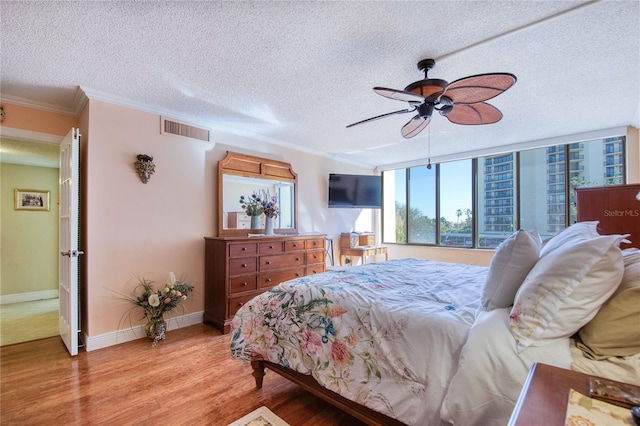 bedroom with ceiling fan, ornamental molding, a textured ceiling, and light hardwood / wood-style flooring