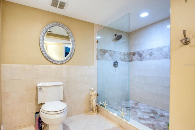 bathroom with tile patterned flooring, toilet, tiled shower, and tile walls