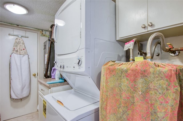 clothes washing area featuring stacked washer and dryer, cabinets, and a textured ceiling