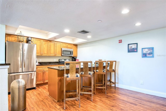 kitchen with a kitchen breakfast bar, crown molding, a kitchen island, light hardwood / wood-style floors, and stainless steel appliances