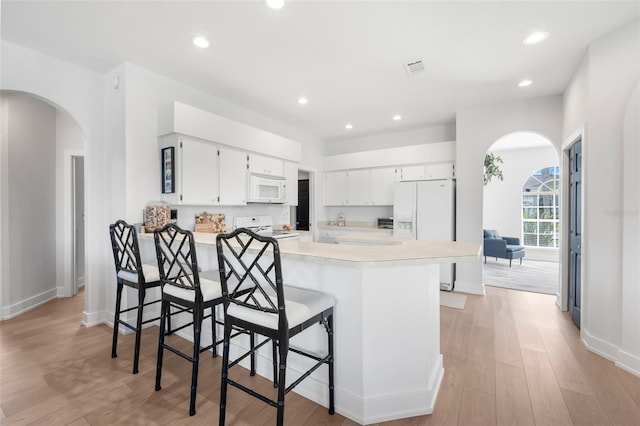 kitchen featuring kitchen peninsula, light hardwood / wood-style floors, white appliances, a kitchen bar, and white cabinets