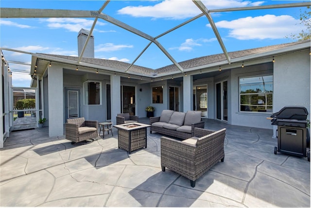 view of patio featuring area for grilling, glass enclosure, and an outdoor living space with a fire pit