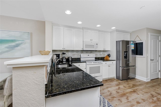 kitchen with white appliances, sink, light hardwood / wood-style flooring, dark stone countertops, and kitchen peninsula