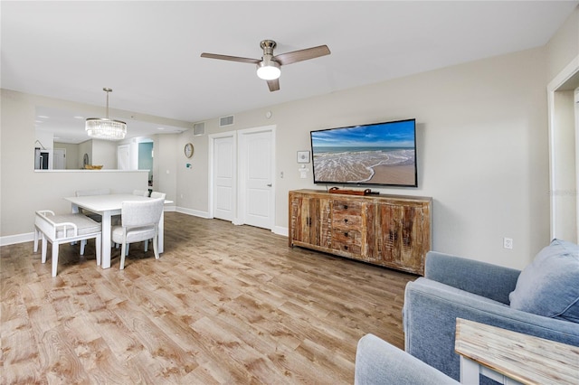 living room with ceiling fan with notable chandelier and light hardwood / wood-style floors