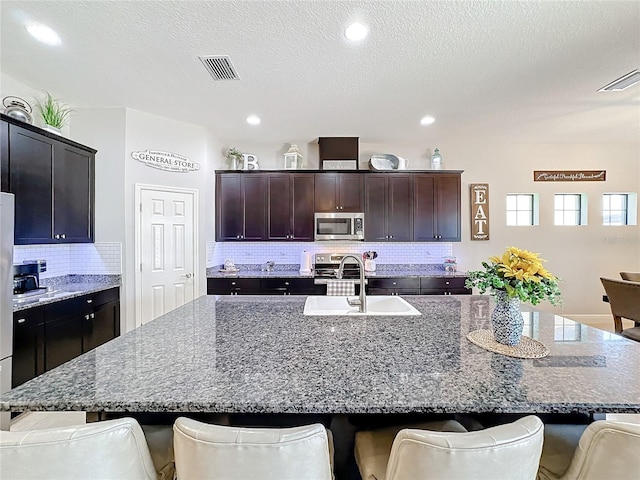 kitchen featuring a kitchen bar, stainless steel appliances, a center island with sink, and sink