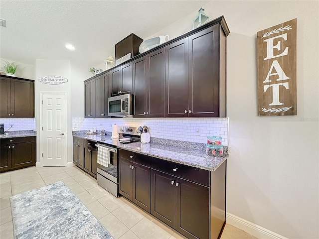 kitchen featuring dark brown cabinetry, light stone countertops, backsplash, light tile patterned floors, and appliances with stainless steel finishes