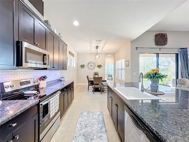 kitchen with sink, dark stone counters, pendant lighting, dark brown cabinets, and appliances with stainless steel finishes