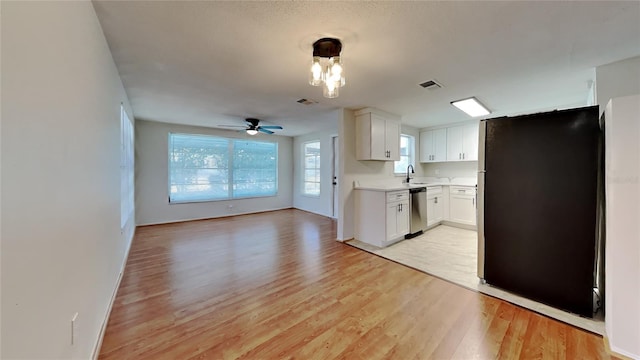 kitchen featuring dishwasher, sink, black fridge, light hardwood / wood-style flooring, and white cabinets