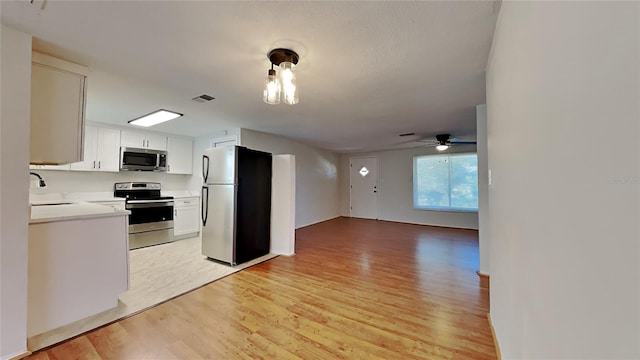 kitchen with appliances with stainless steel finishes, light wood-type flooring, ceiling fan, sink, and white cabinets