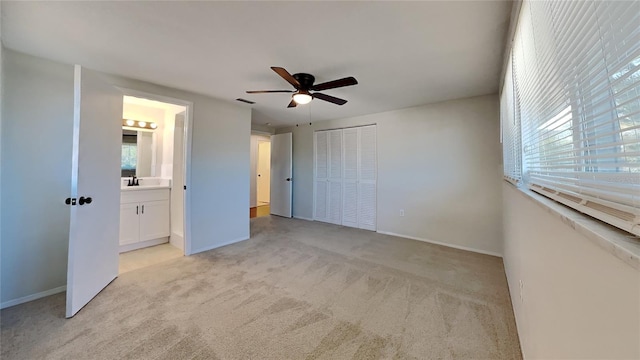 unfurnished bedroom featuring multiple windows, ceiling fan, ensuite bath, and light carpet