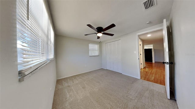 unfurnished bedroom featuring multiple windows, light carpet, a closet, and ceiling fan