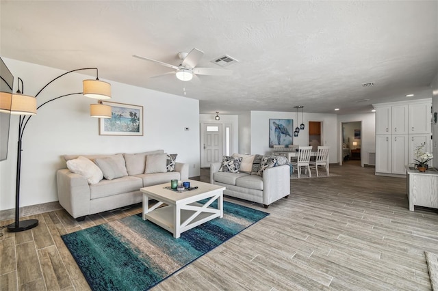 living room featuring ceiling fan, light hardwood / wood-style floors, and a textured ceiling