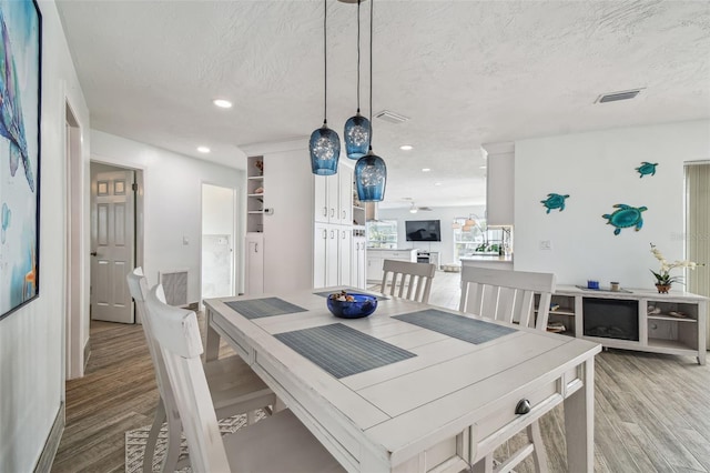 dining area featuring built in shelves, ceiling fan, a textured ceiling, and light hardwood / wood-style flooring