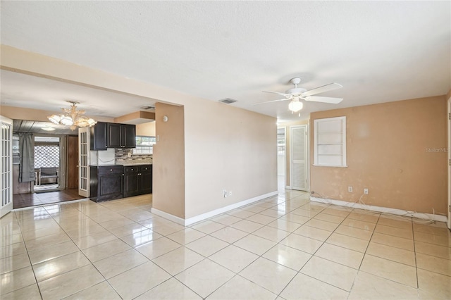 spare room featuring plenty of natural light, light tile patterned floors, and ceiling fan with notable chandelier