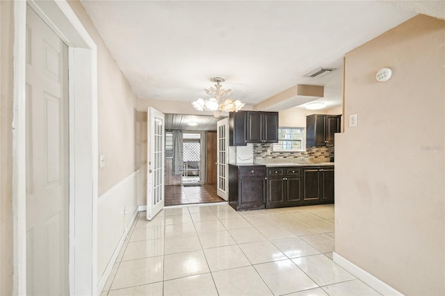 kitchen with a notable chandelier, dark brown cabinets, light tile patterned floors, and a wealth of natural light