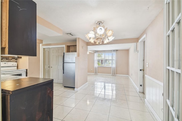 kitchen with decorative backsplash, white range oven, light tile patterned floors, an inviting chandelier, and stainless steel refrigerator