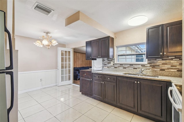 kitchen featuring stainless steel refrigerator, sink, tasteful backsplash, a chandelier, and electric stove