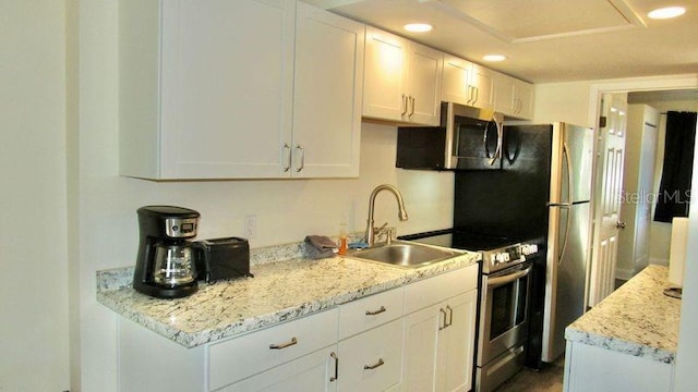 kitchen with white cabinets, stainless steel appliances, light stone counters, and sink