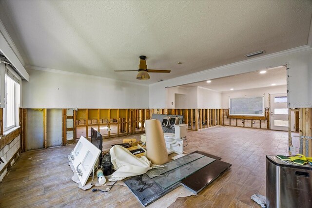 misc room with a textured ceiling, ceiling fan, wooden walls, crown molding, and hardwood / wood-style flooring