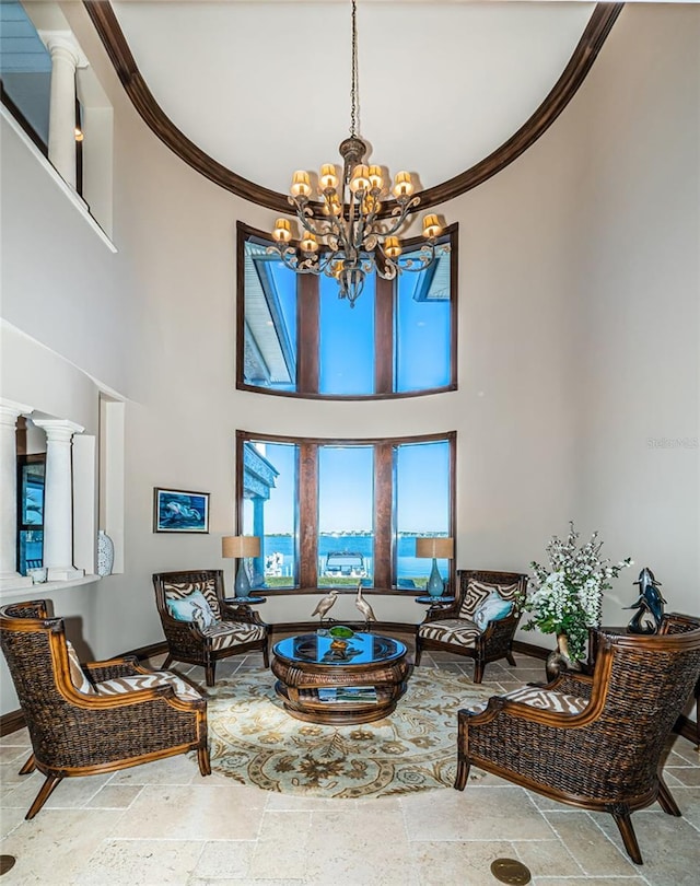 living room with a notable chandelier, a towering ceiling, crown molding, and decorative columns