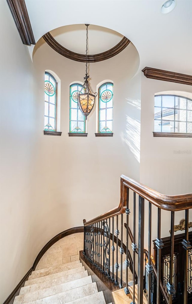 staircase featuring plenty of natural light, wood-type flooring, ornamental molding, and a chandelier