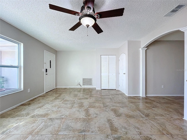 spare room with a textured ceiling, decorative columns, ceiling fan, and a healthy amount of sunlight