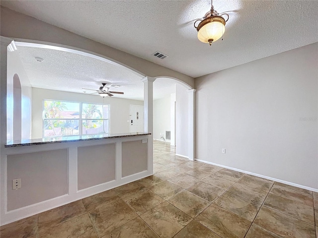 empty room featuring a textured ceiling, ornate columns, and ceiling fan