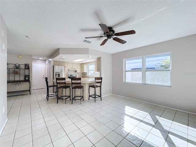 kitchen with stainless steel refrigerator with ice dispenser, a kitchen breakfast bar, a textured ceiling, light tile patterned floors, and white cabinets