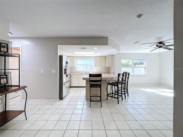 kitchen with stainless steel refrigerator with ice dispenser, a textured ceiling, light tile patterned floors, and ceiling fan