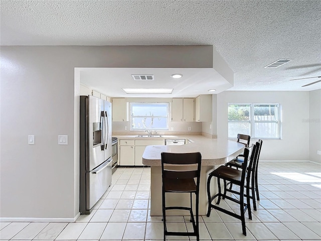 kitchen with a breakfast bar, light tile patterned floors, a textured ceiling, kitchen peninsula, and stainless steel appliances