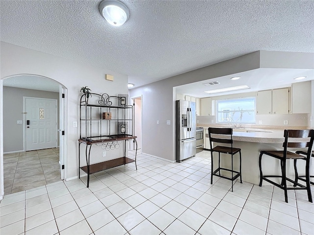 kitchen with a kitchen breakfast bar, light tile patterned floors, a textured ceiling, and appliances with stainless steel finishes