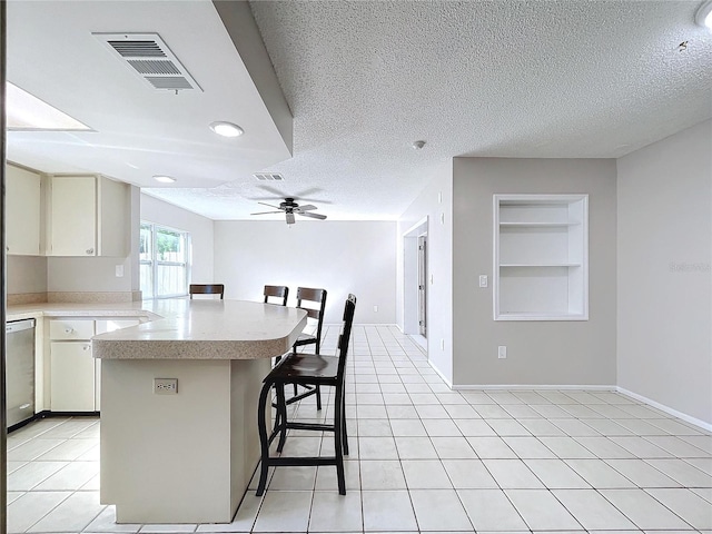 kitchen featuring a kitchen bar, ceiling fan, stainless steel dishwasher, and a textured ceiling