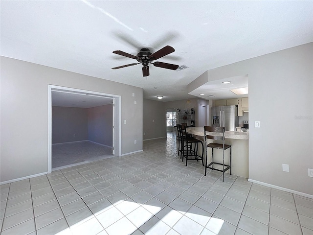 kitchen featuring stainless steel fridge, light tile patterned floors, ceiling fan, and a kitchen breakfast bar