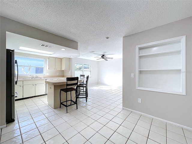 kitchen with white cabinets, a kitchen bar, a textured ceiling, and stainless steel refrigerator