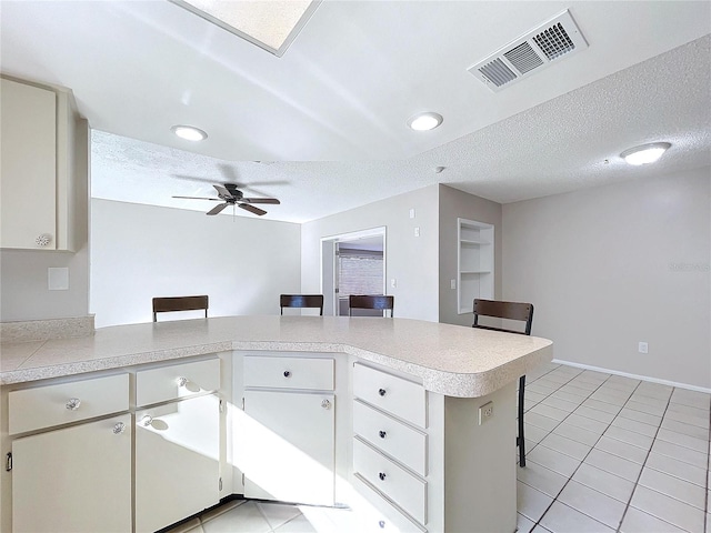 kitchen featuring a kitchen bar, kitchen peninsula, ceiling fan, and a textured ceiling