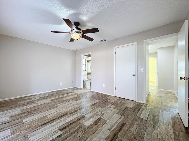 unfurnished bedroom featuring a textured ceiling, light hardwood / wood-style floors, ensuite bath, and ceiling fan