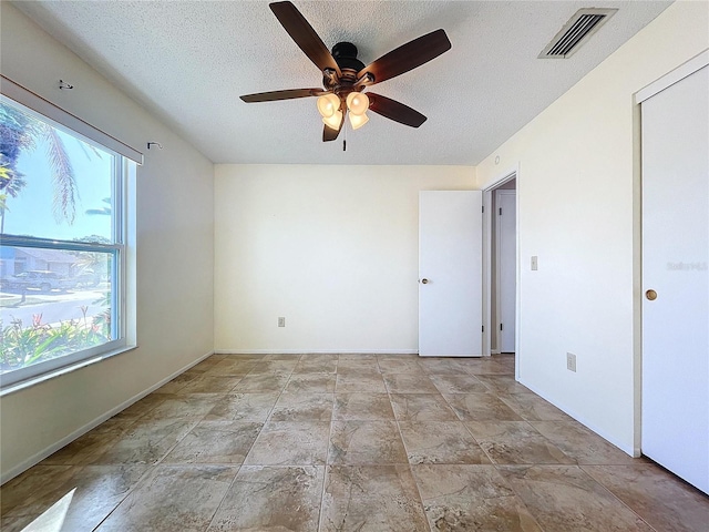 empty room with ceiling fan, plenty of natural light, and a textured ceiling