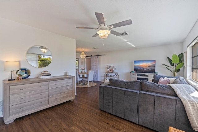 living room with a barn door, ceiling fan, and dark wood-type flooring