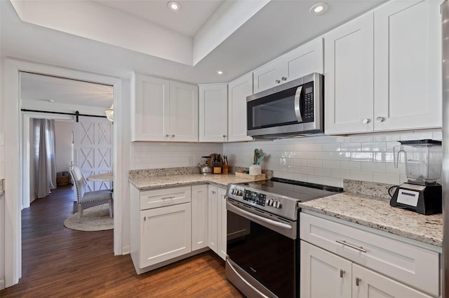 kitchen with white cabinetry, stainless steel appliances, a barn door, dark hardwood / wood-style flooring, and decorative backsplash